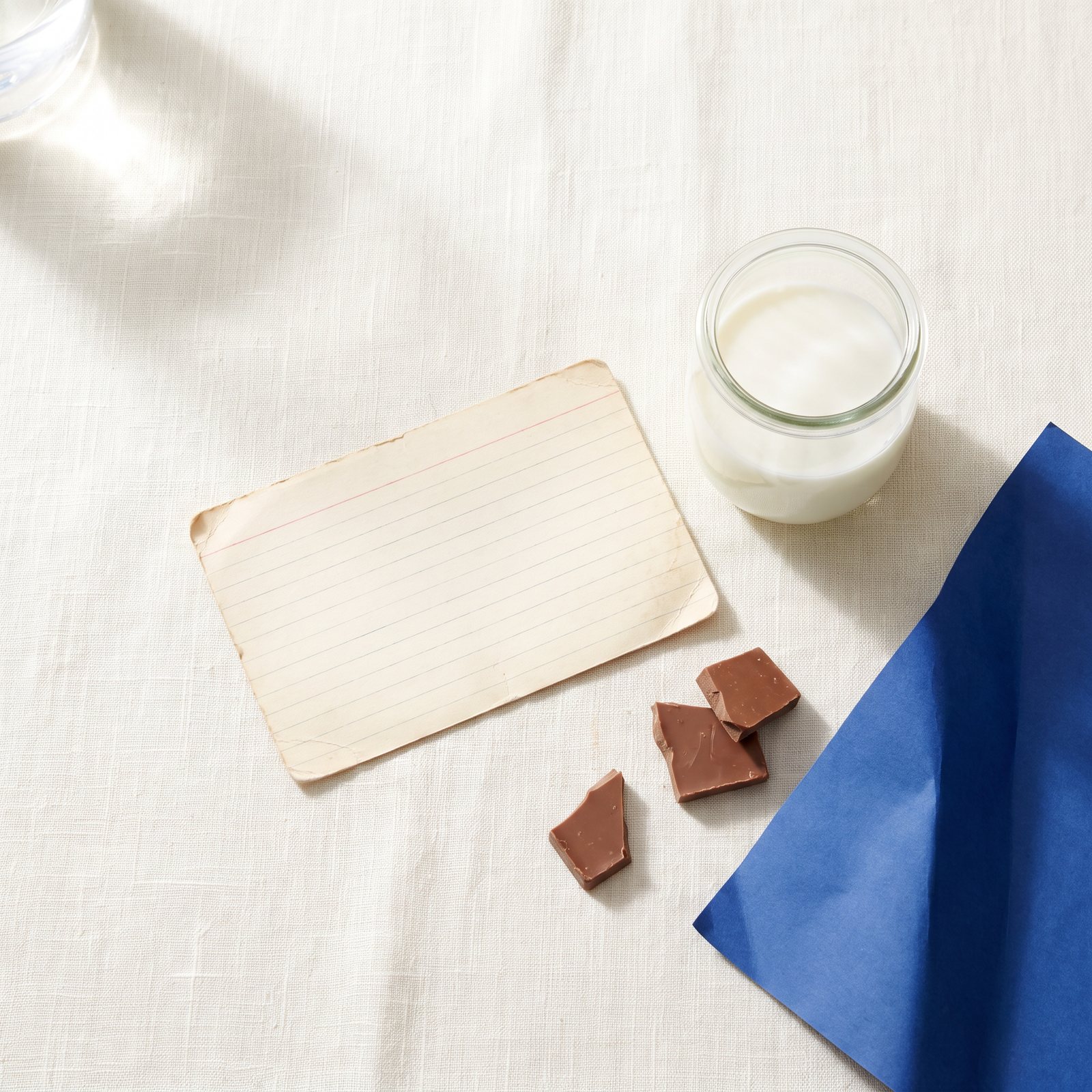 An aged recipe card beside fresh milk and broken chocolate